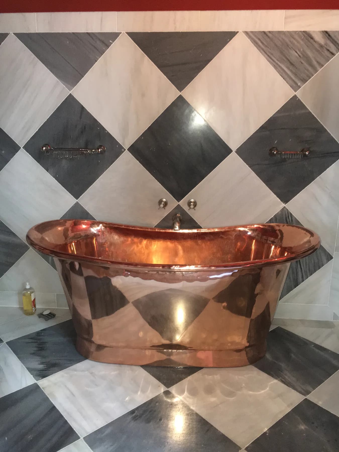 Baignoire îlot en cuivre poli devant un mur en marbre damier noir et blanc